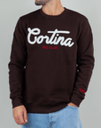 Felpa Superculture Girocollo Cortina Ski Club indossata da uomo, colore marrone scuro, con logo bianco e rosso.
