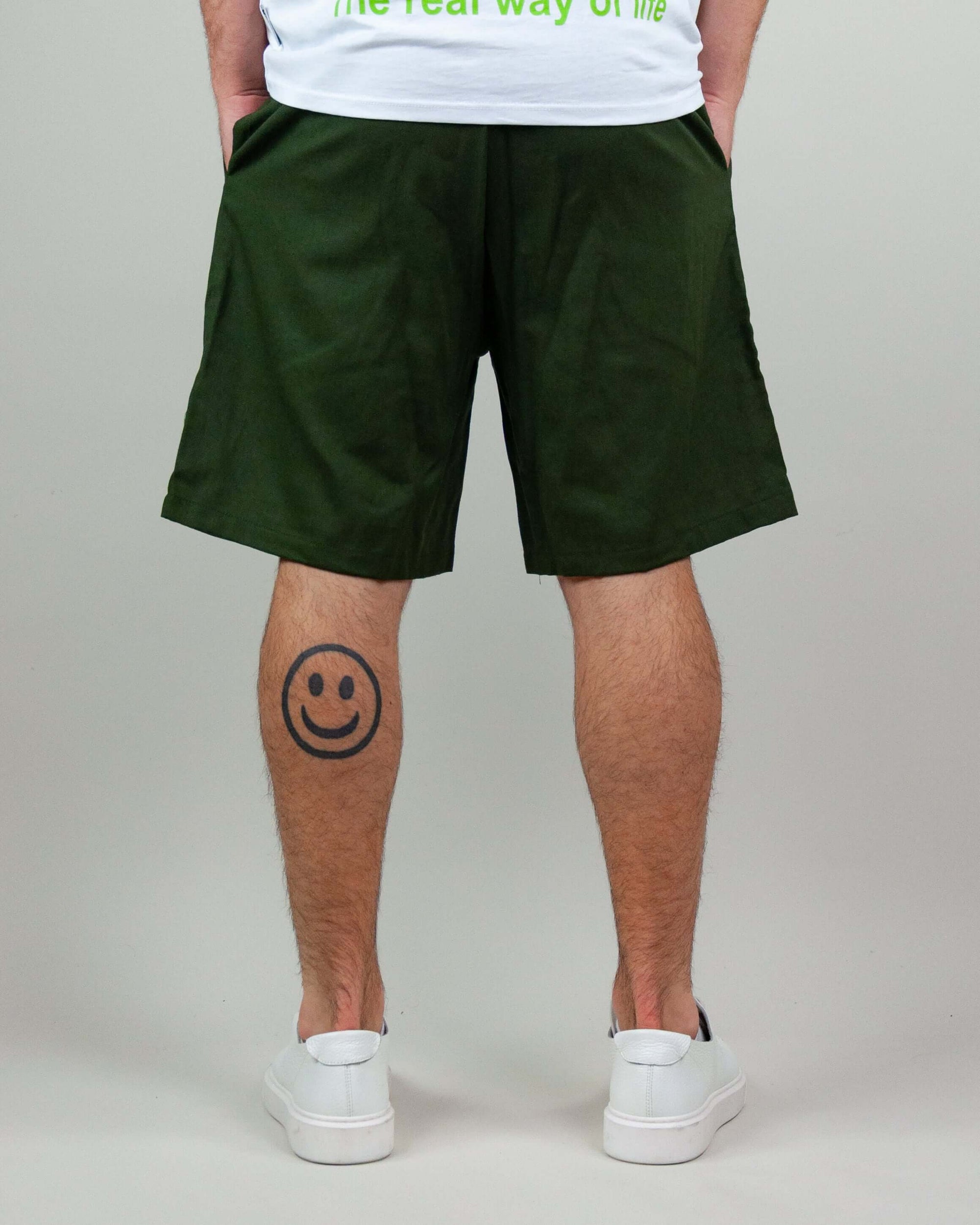 Man wearing green Bermuda shorts with a smiley face tattoo on his calf.