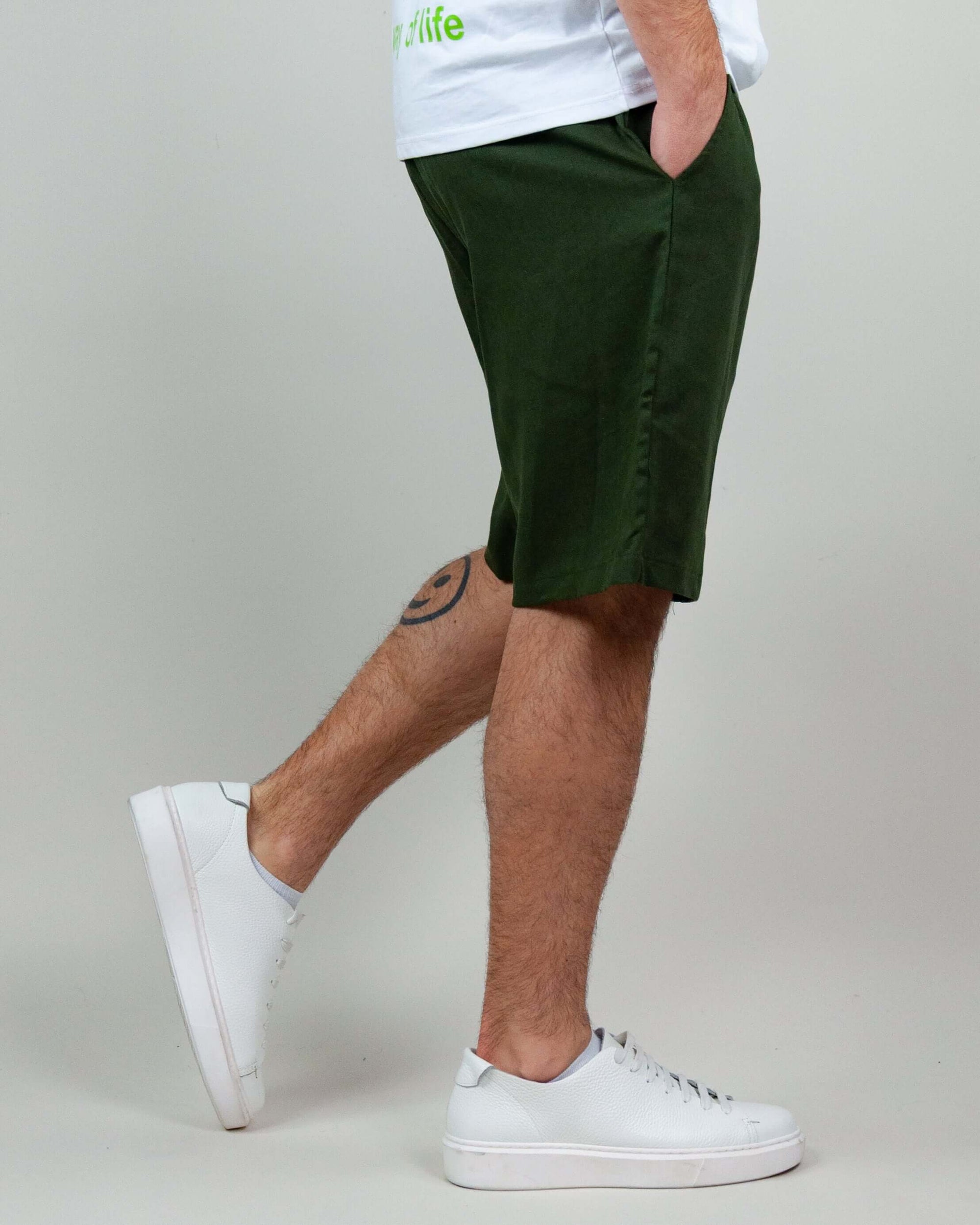 Bermuda Corfu in green linen-rayon blend, styled with white sneakers and visible tattoo on the leg.