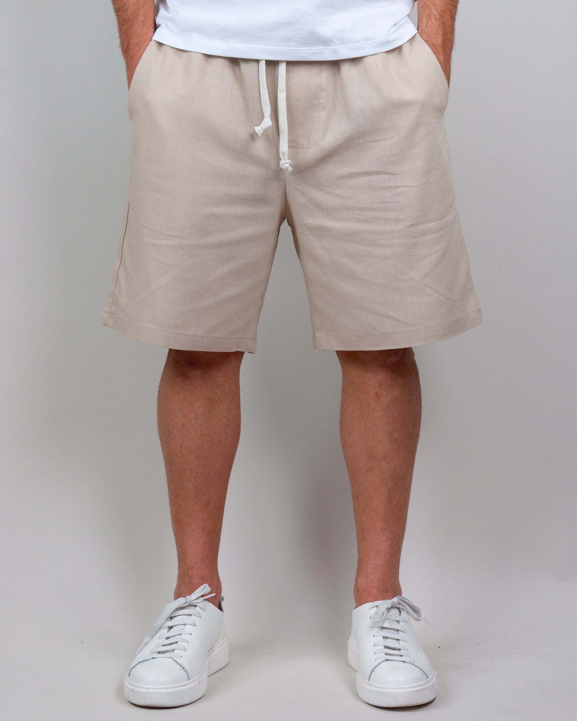 Bermuda shorts in light beige with drawstring, styled with a casual white t-shirt and sneakers.