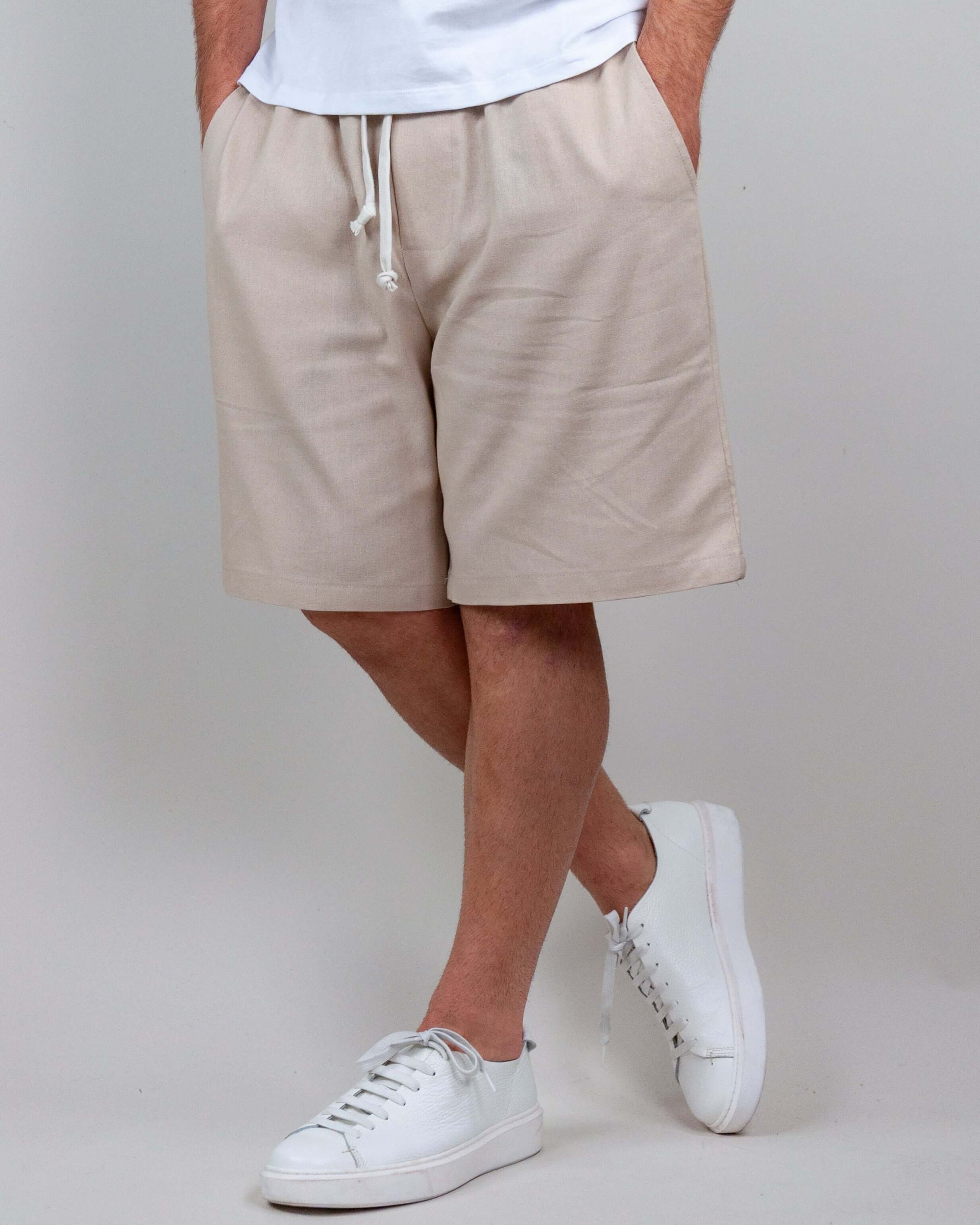 Man wearing beige Bermuda shorts made of linen and rayon, styled with white sneakers and casual t-shirt.