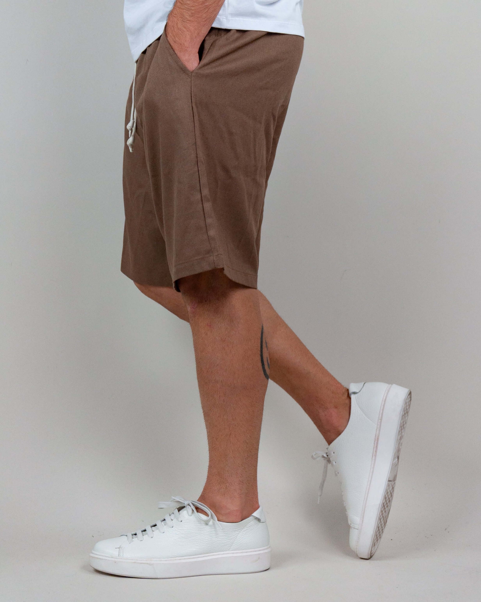 Side view of a man wearing brown Bermuda shorts with a white t-shirt and stylish white sneakers.