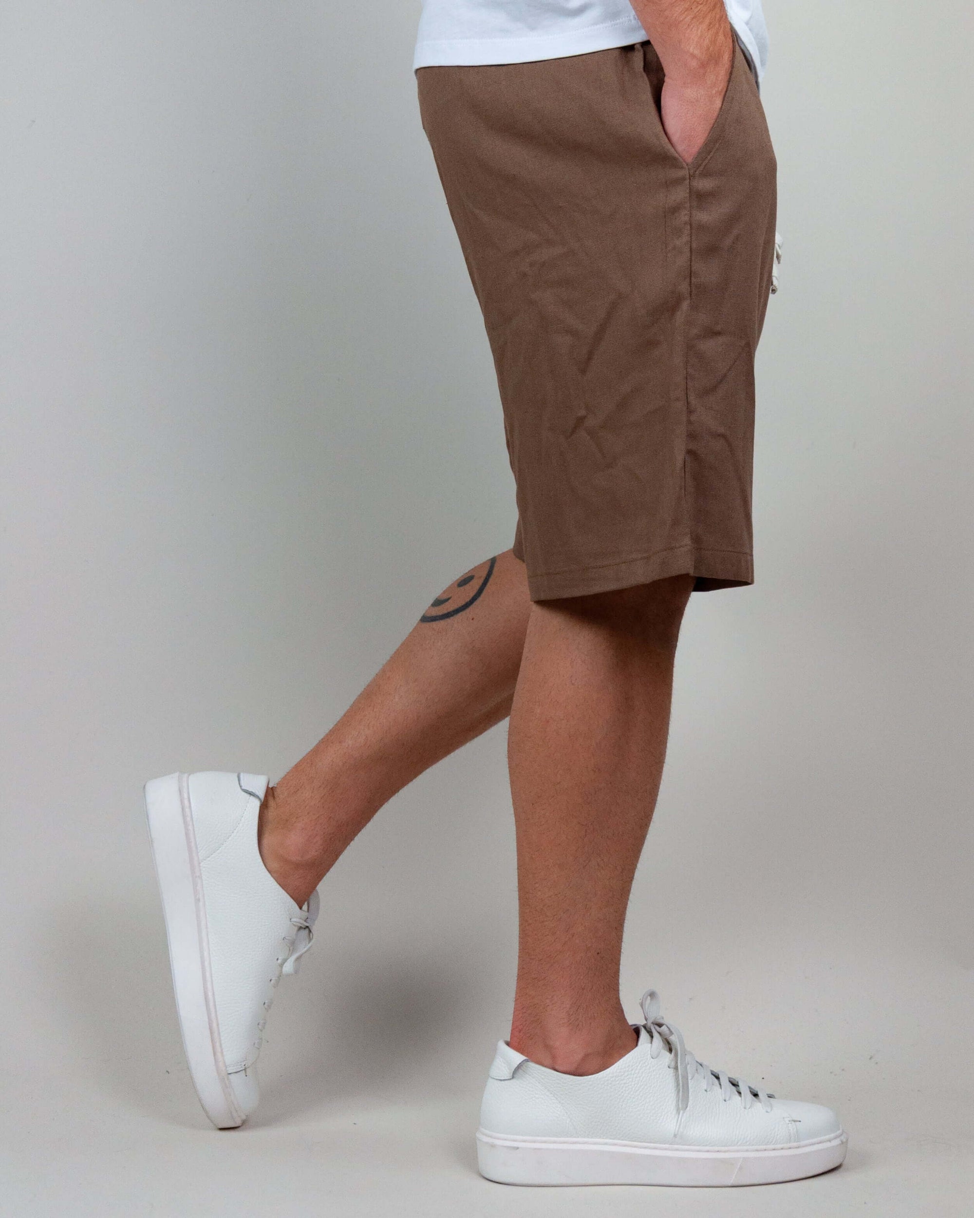 Side view of Bermuda shorts in brown, styled with white sneakers for a casual look.