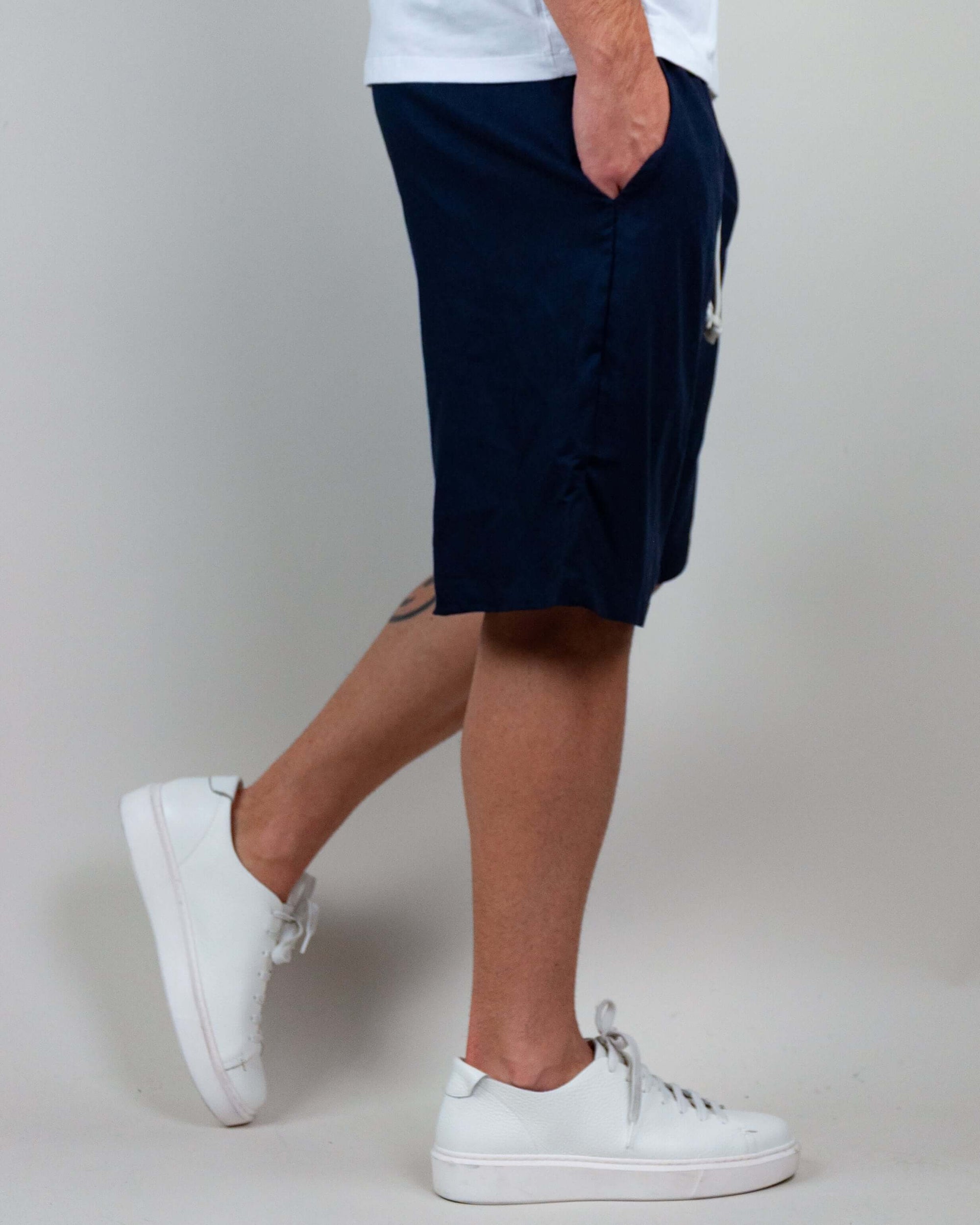 Man wearing navy Bermuda shorts with pockets, paired with white sneakers, showcasing comfort and style.