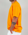Model wearing a bright orange T-shirt, 100% cotton, semi-over fit, showcasing a stylish streetwear look.