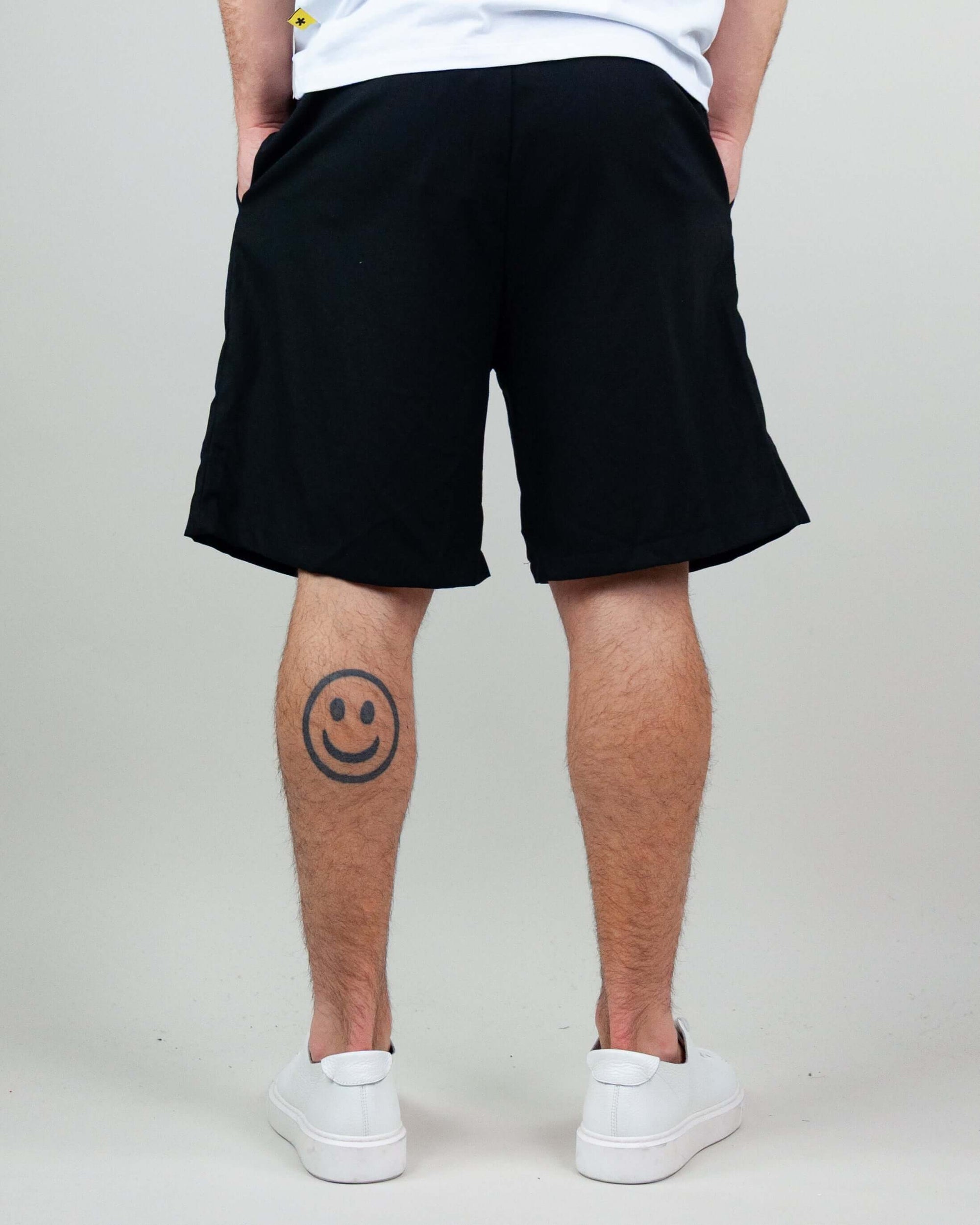Back view of bermuda shorts, showcasing a relaxed fit and a smiley tattoo on the leg.