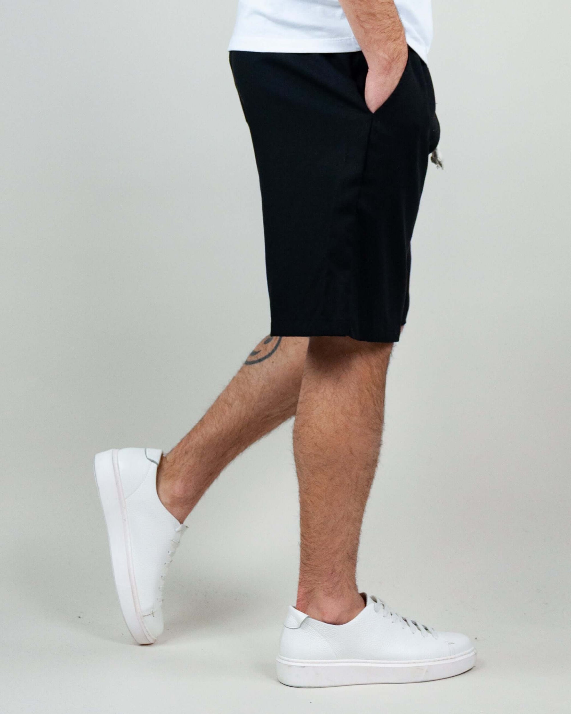 Model wearing Bermuda shorts in black with white sneakers, showcasing modern style and comfort.