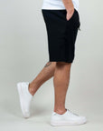 Model wearing Bermuda shorts in black with white sneakers, showcasing modern style and comfort.