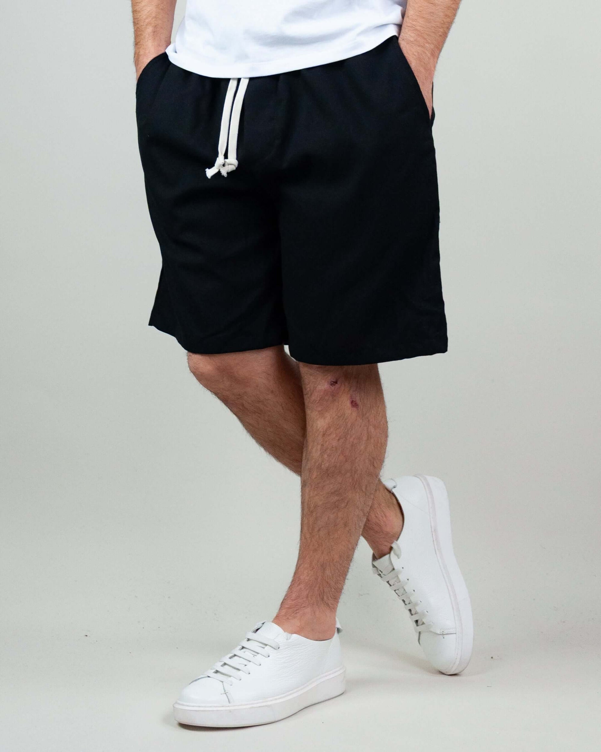 Bermuda shorts in black fabric with drawstring, styled with white sneakers for a casual summer look.