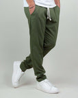Pantaloni sportivi uomo in misto lino e rayon, colore verde, con tasche e cintura elastica, abbinati a sneakers bianche.