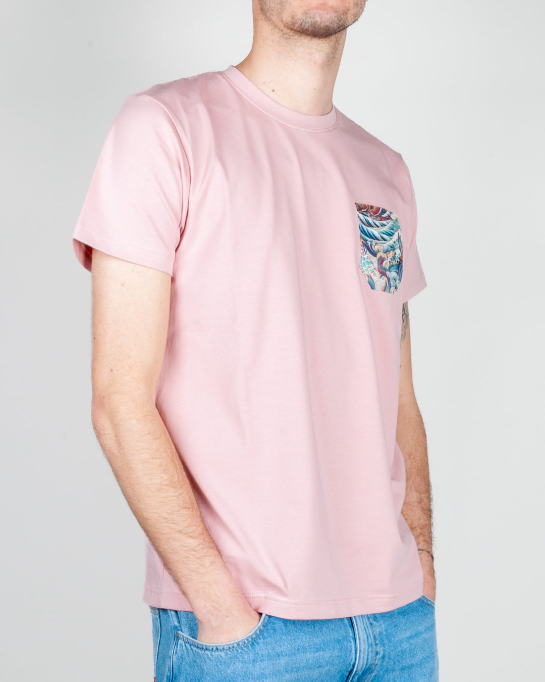 Un giovane indossa un T-shirt taschino V2 Art. TUCL con una tasca decorativa e una tonalità rosa.