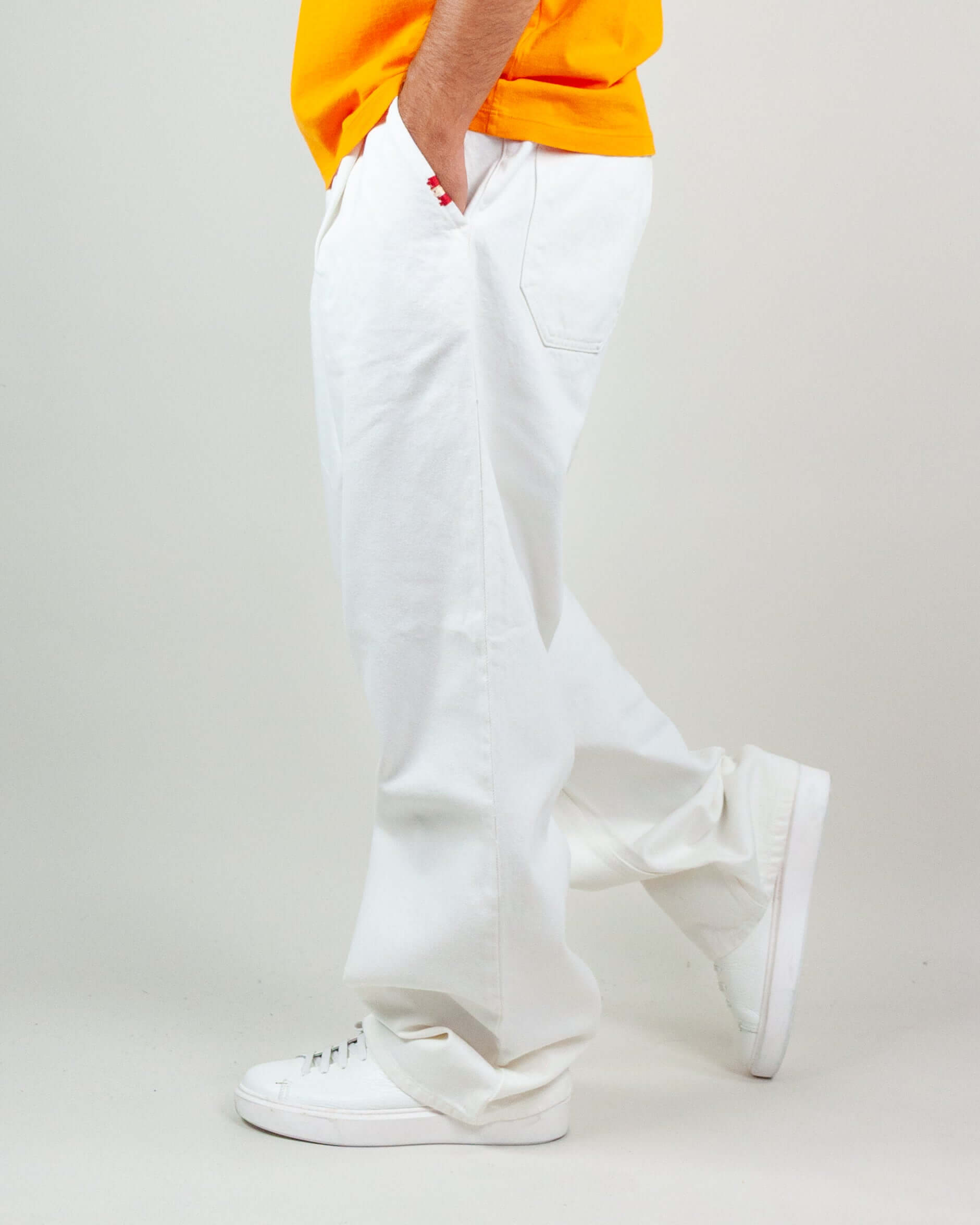 Side view of a man wearing white twill pants with pockets, paired with a bright yellow t-shirt and white sneakers.