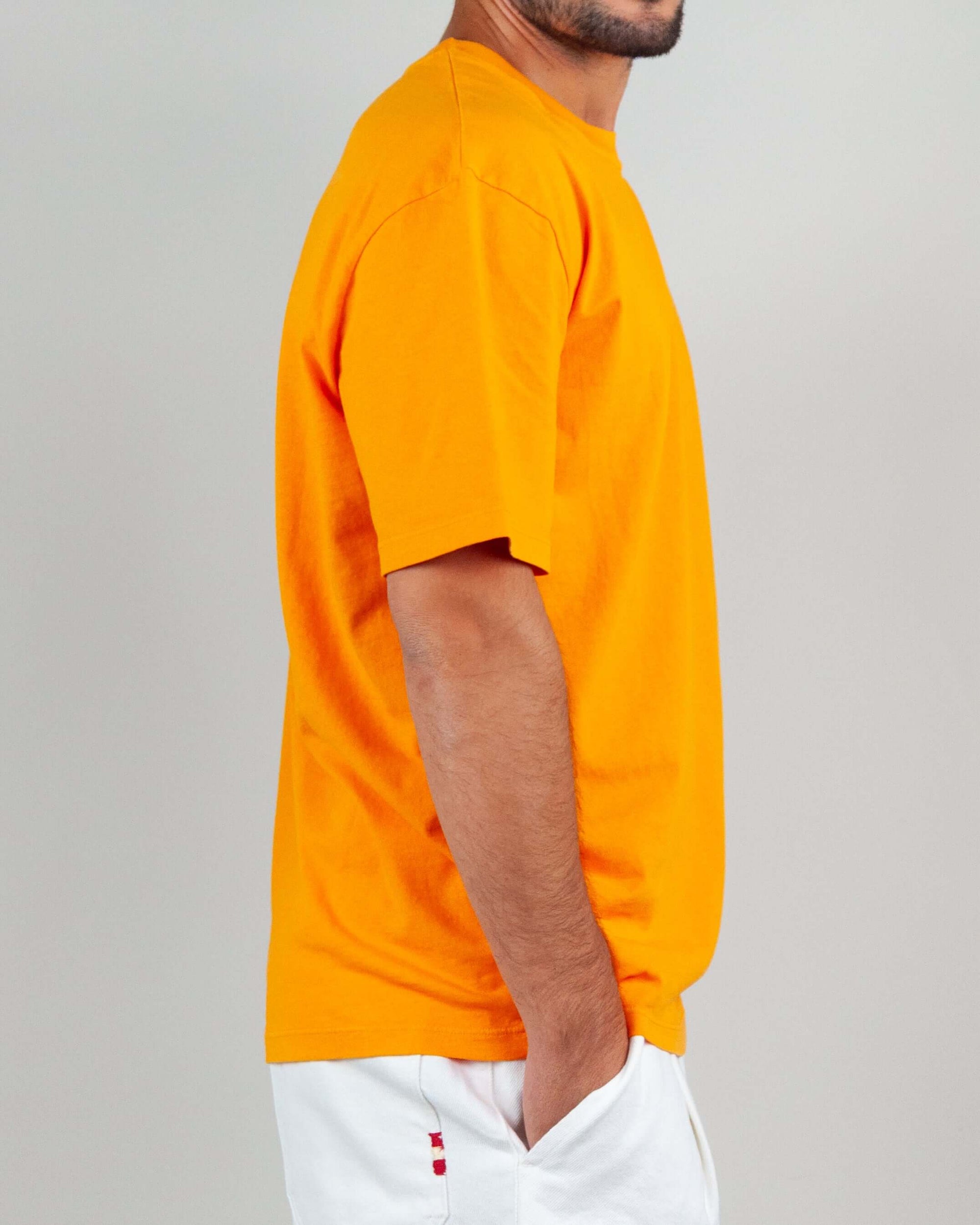 Side view of a man wearing an orange semi-over T-shirt made of 100% cotton.