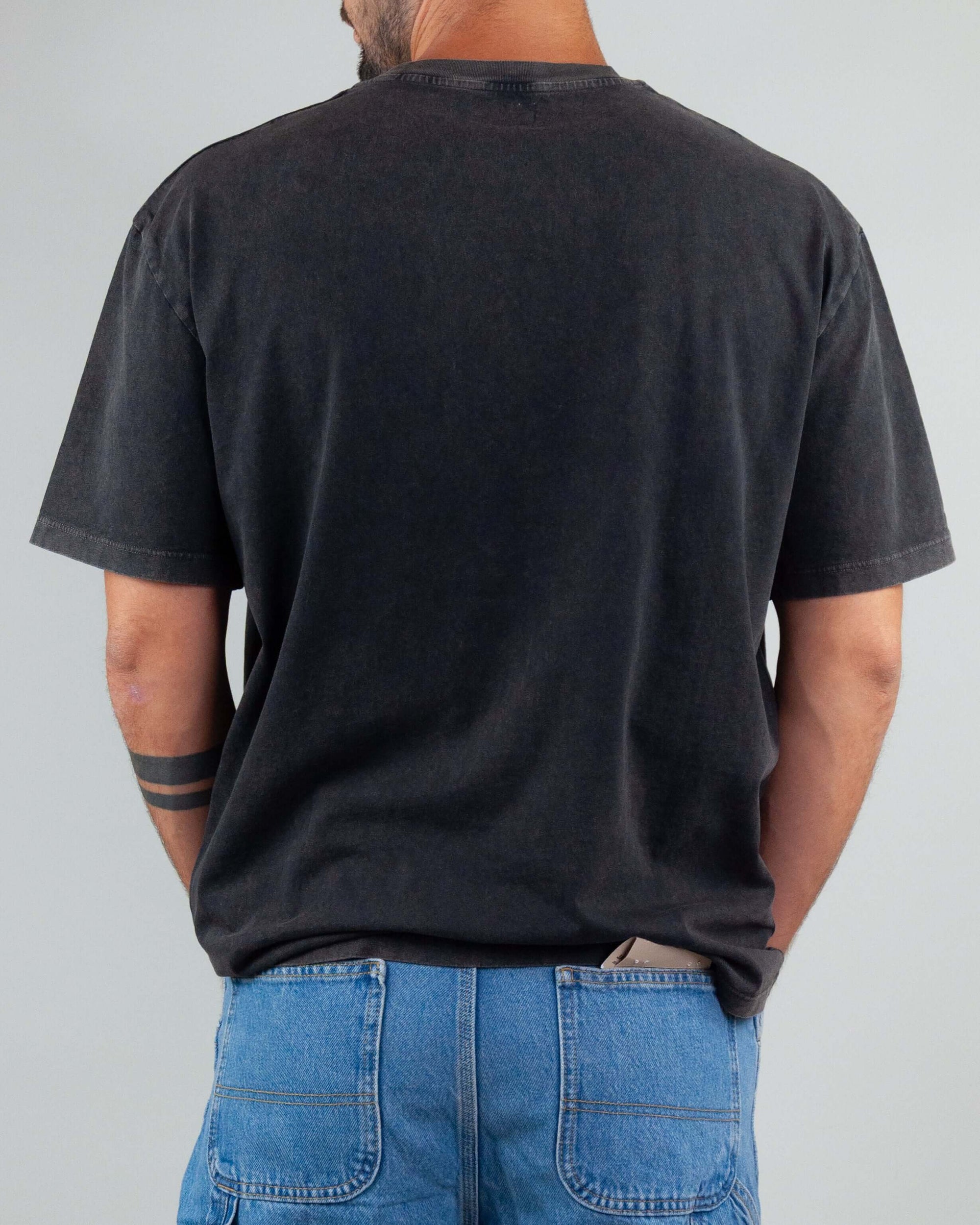Back view of a man wearing a black T-shirt with Amish art micro logo and denim shorts, showcasing the semi-over fit.