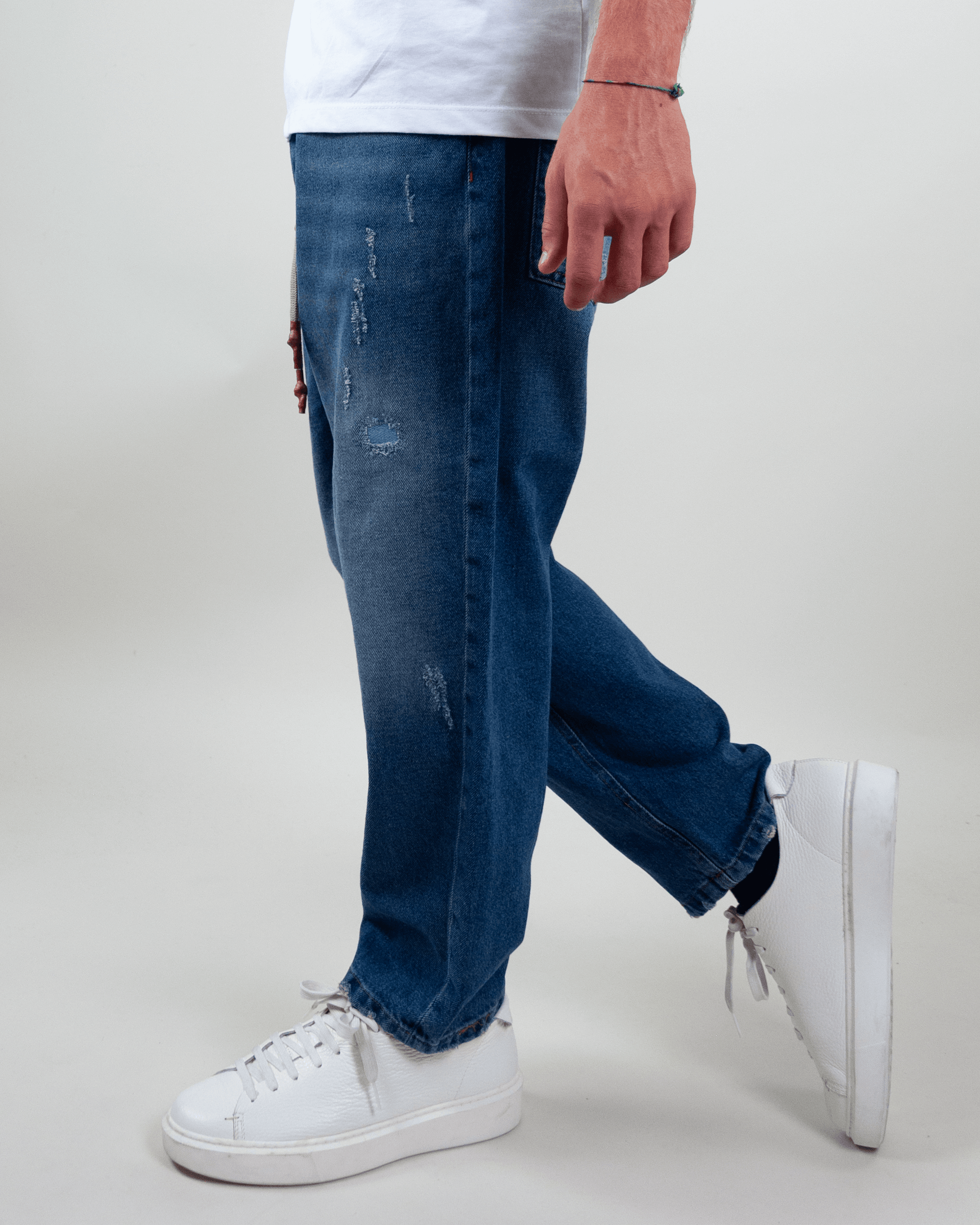 Man wearing Jeans Coulisse Uomo with distressed details and white sneakers.