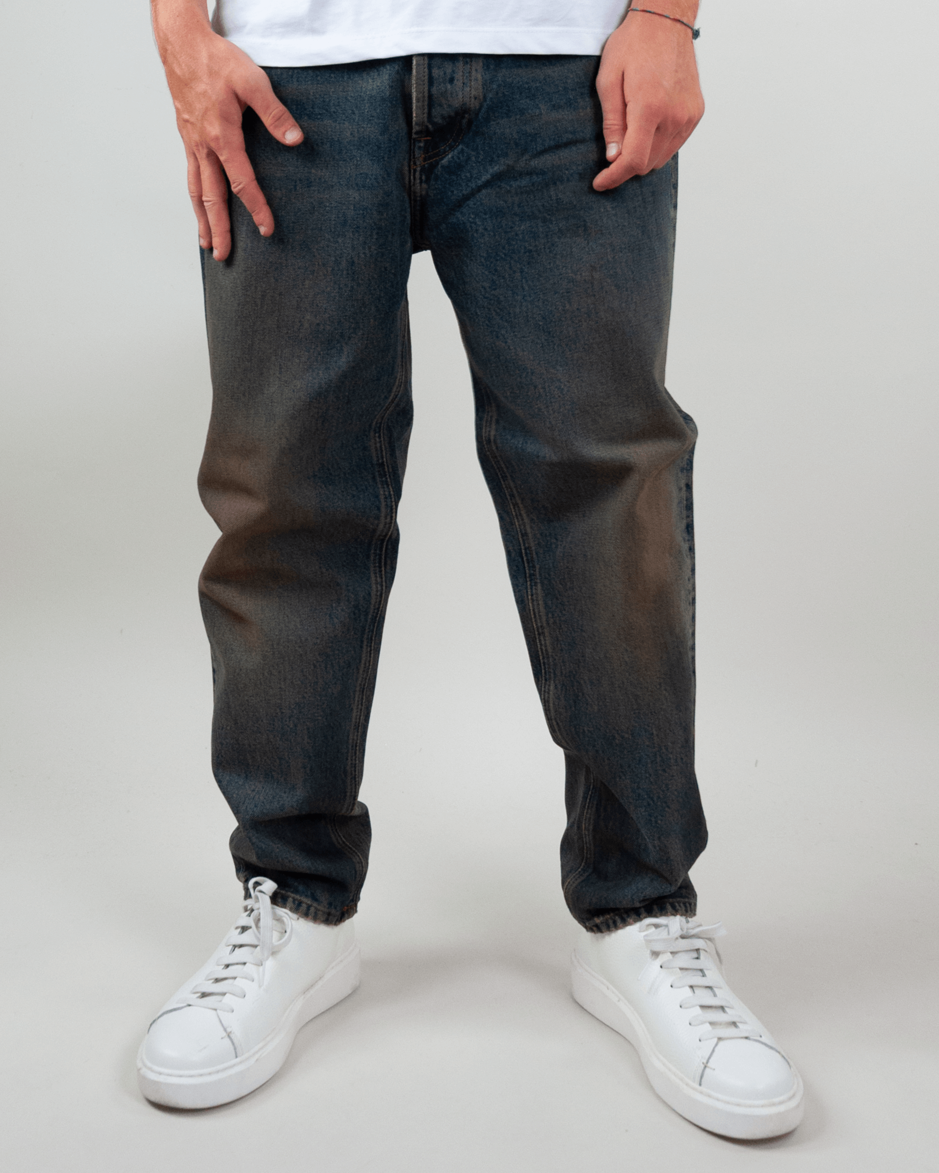 Amish Jeremiah Green dirty denim jeans worn by model with white sneakers standing on neutral background.