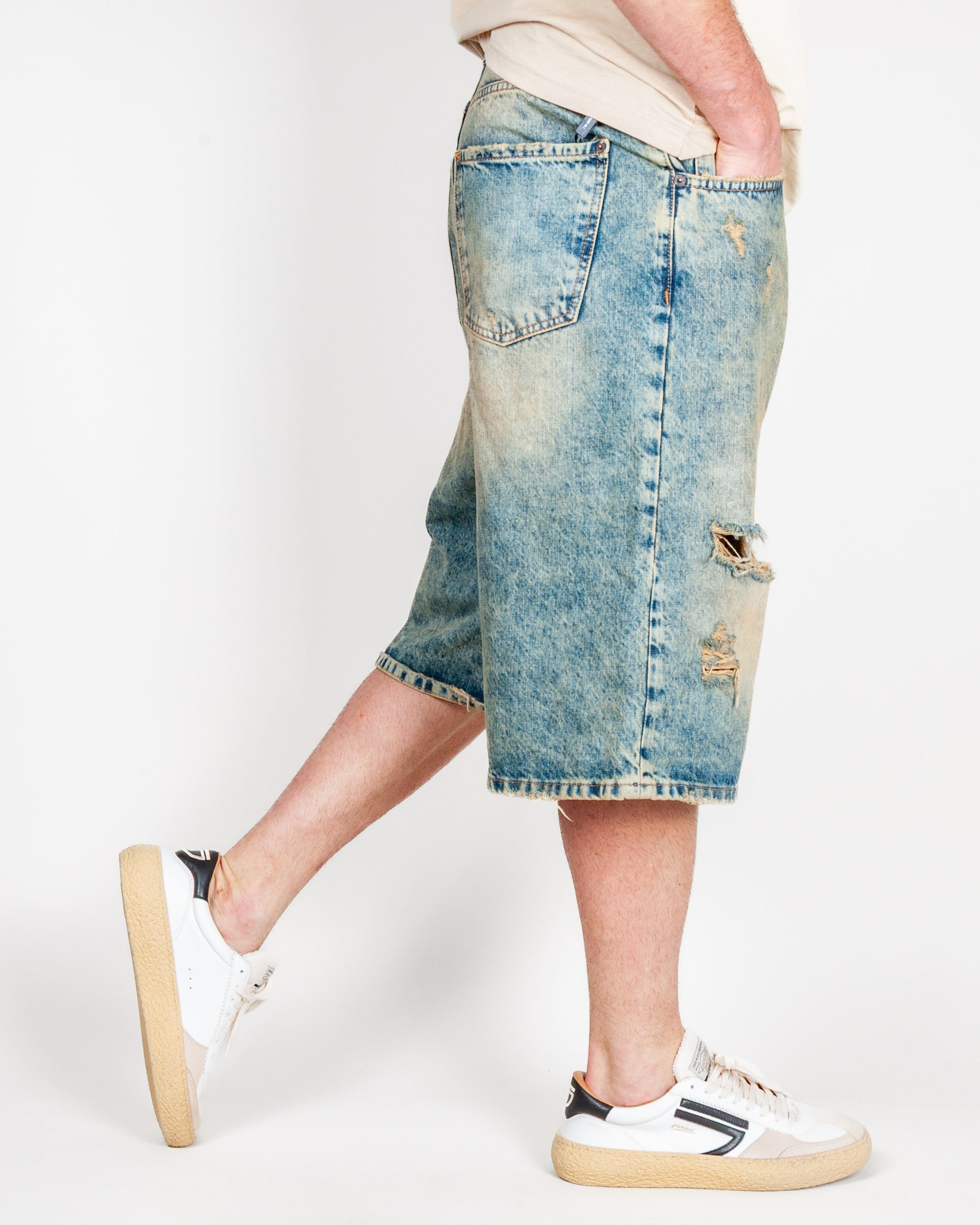 Bermuda Ampio in Denim I'm Brian worn by model, showcasing the distressed denim style, paired with white sneakers.