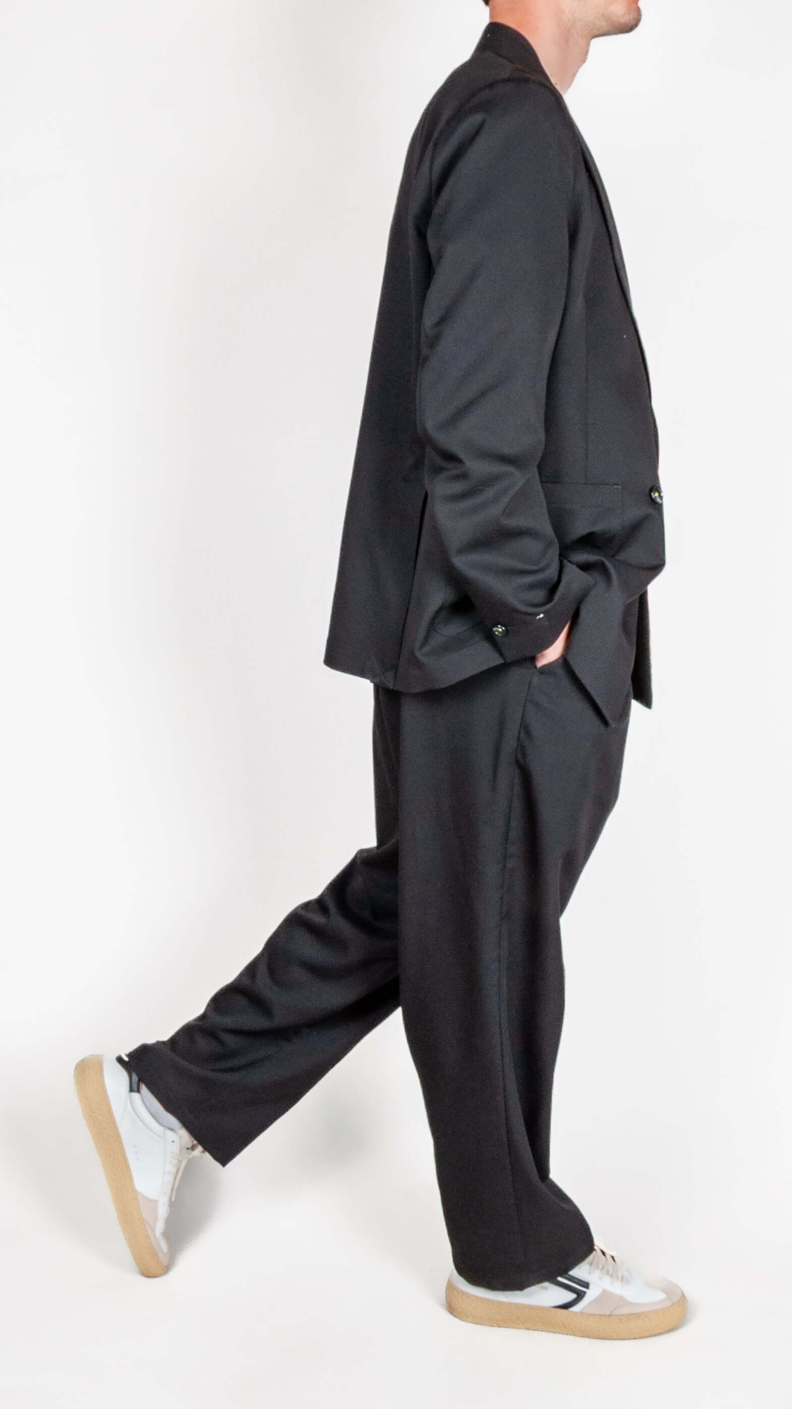 Uomo in abito doppiopetto Berna nero con scarpe sportive, mostra il lato del completo elegante.