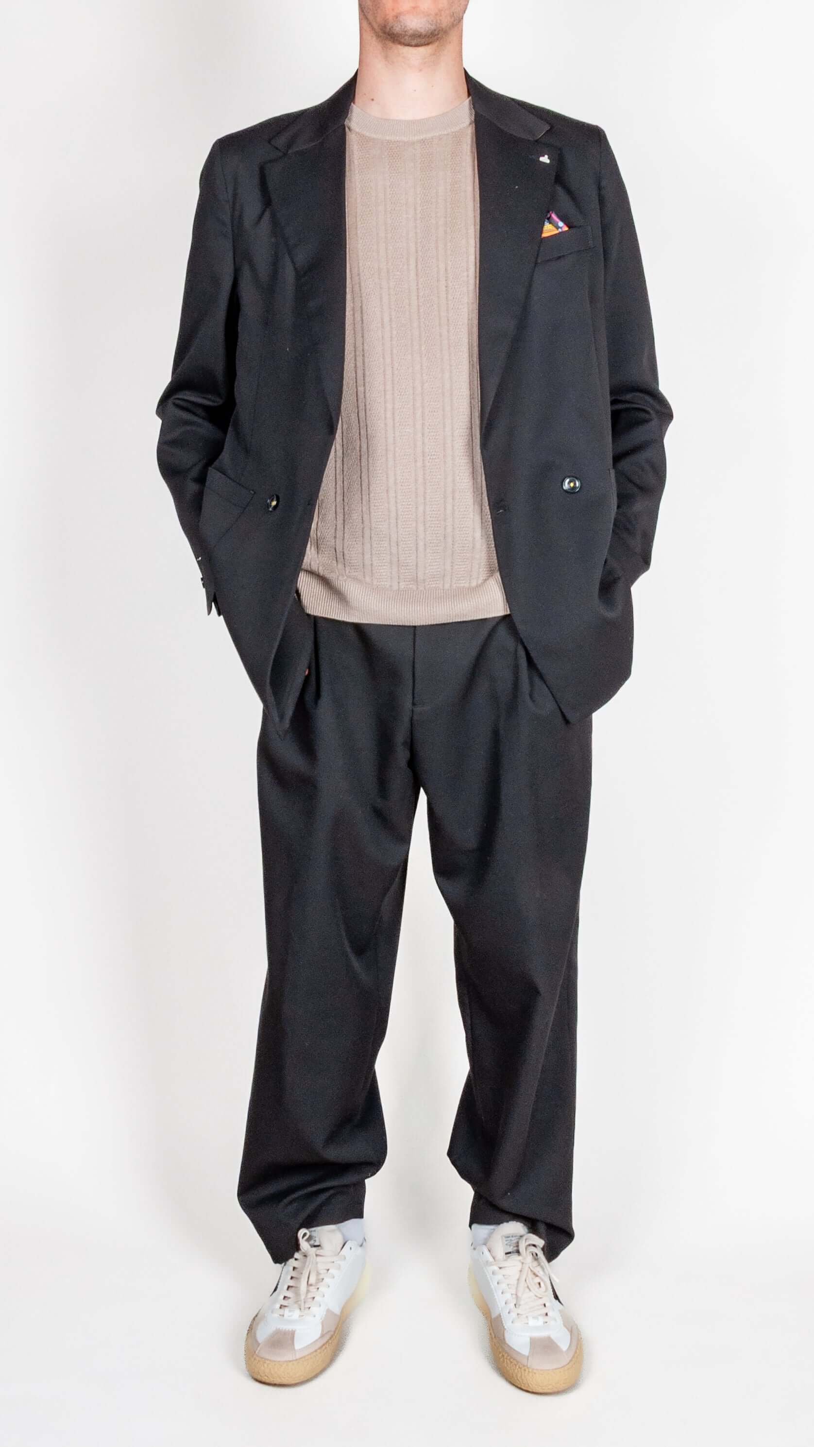 Abito doppiopetto Berna nero worn by a man, styled with a beige sweater and casual sneakers.