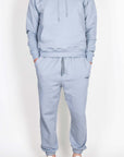 Completo Felpa Superculture grigio: uomo in felpa e pantaloni coordinati grigi, con cappuccio e tasche.