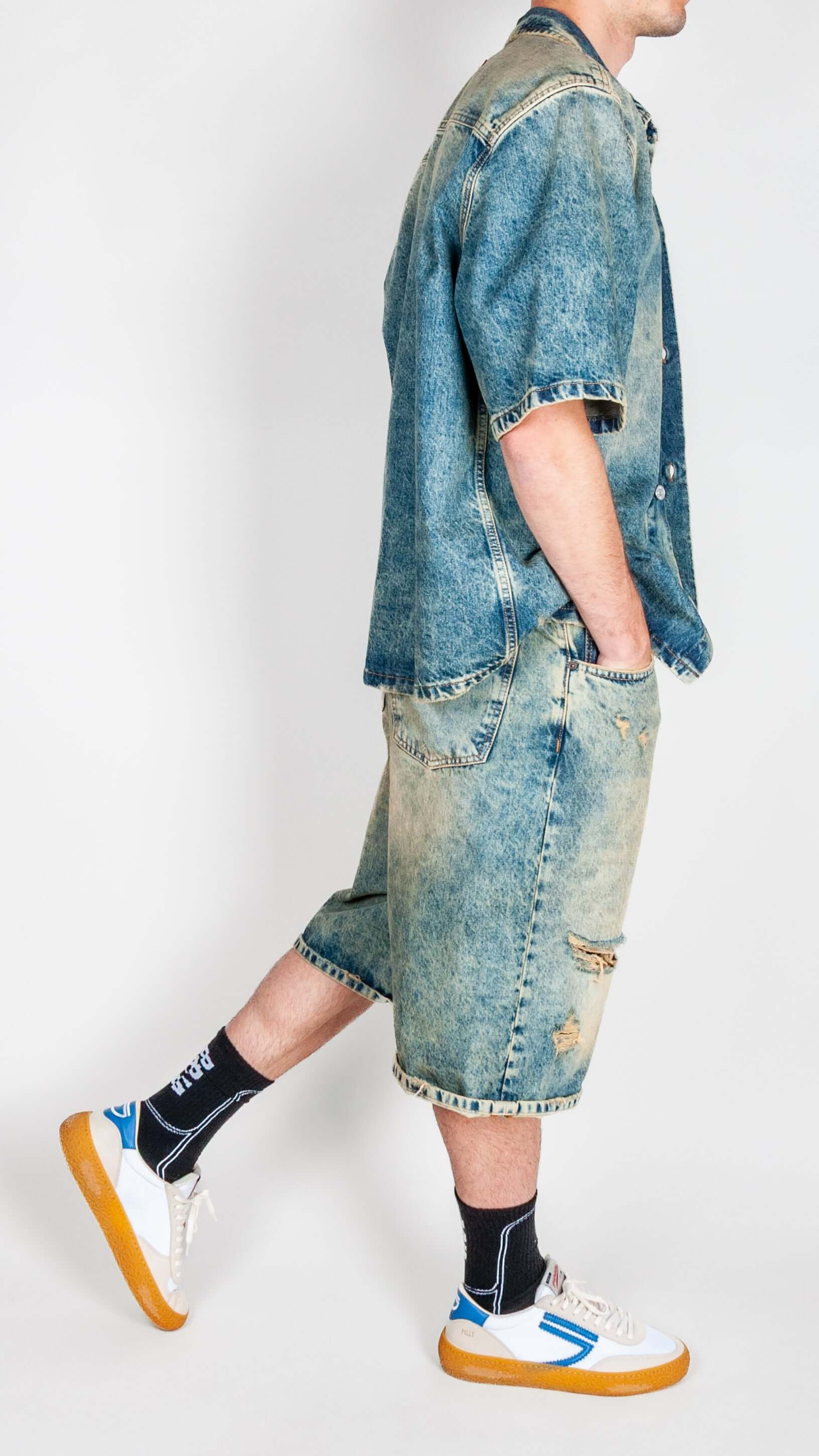 Completo in denim worn by a model, featuring a denim shirt and shorts, paired with trendy sneakers.
