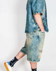 Completo in denim worn by a model, featuring a denim shirt and shorts, paired with trendy sneakers.
