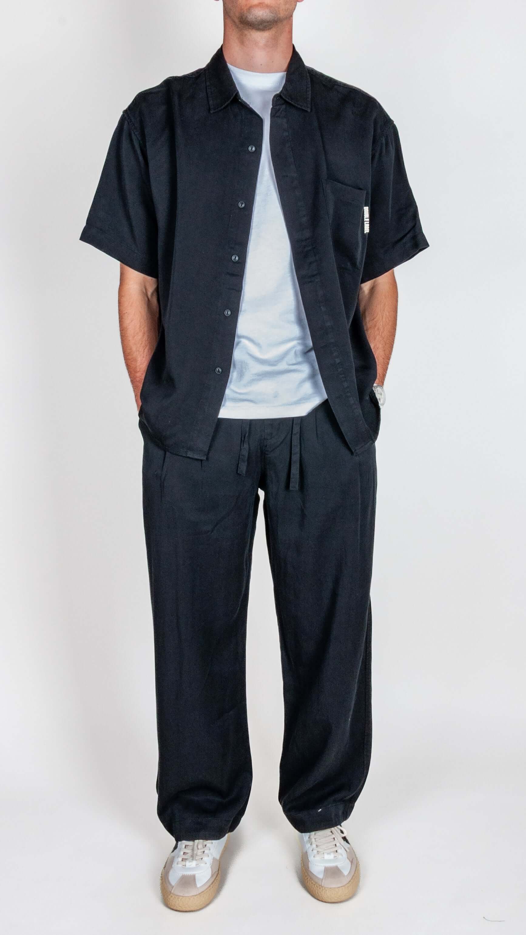 Completo in Lyocell Double Label Nero displayed on a model in a black shirt and pants paired with a light t-shirt.