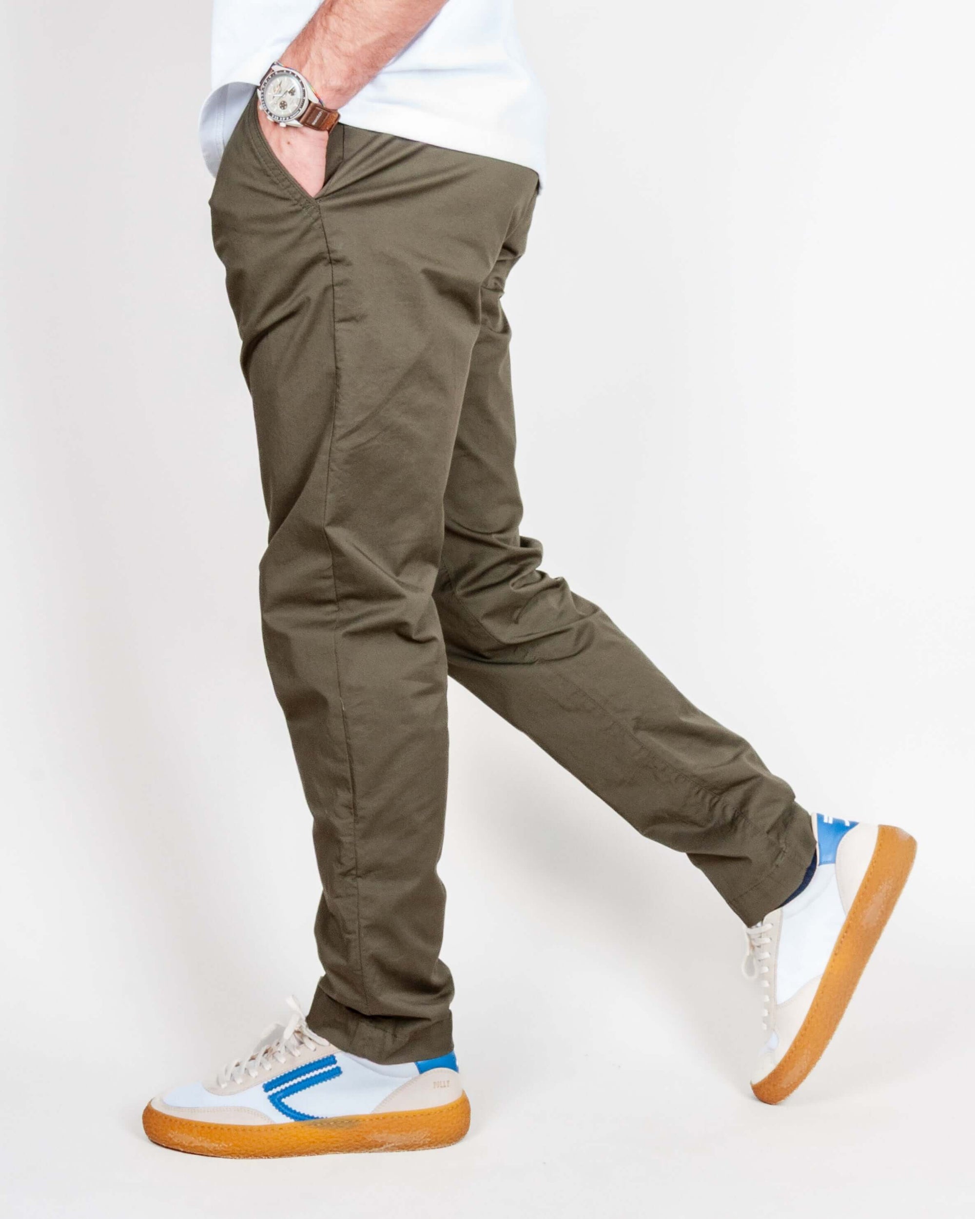 Uomo in pantalone slim fit cotone color oliva, indossato con scarpe bianche e blu.