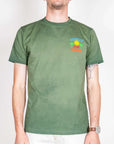 Model wearing T-shirt Fade SuperCulture Sunset Club Paradise Art in green, size L, showcasing vibrant graphic design.